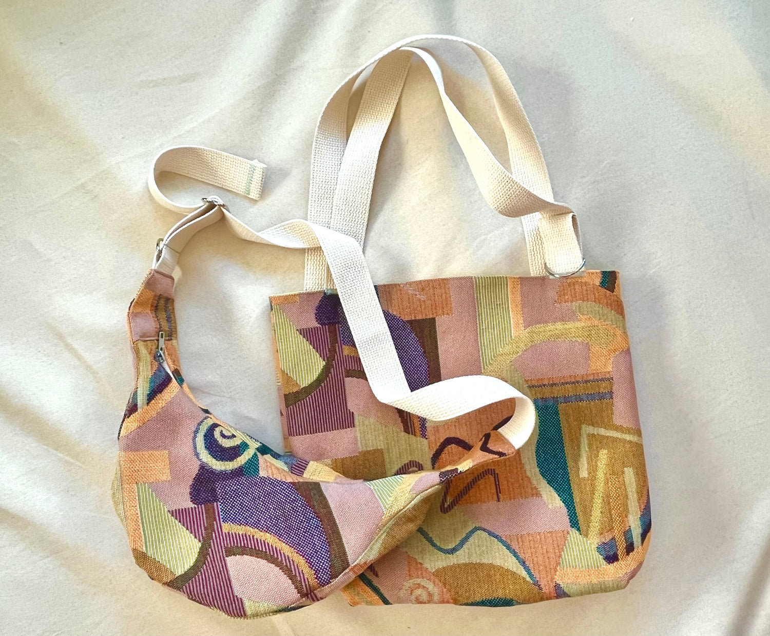 A cross-body sling bag and a double handle tote bag made of abstract multicolor fabric, on a plain canvas background. 